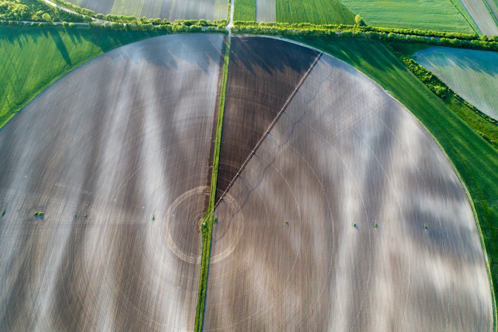 Aerial image of center pivot irrigation system working on round field at sunset in spring